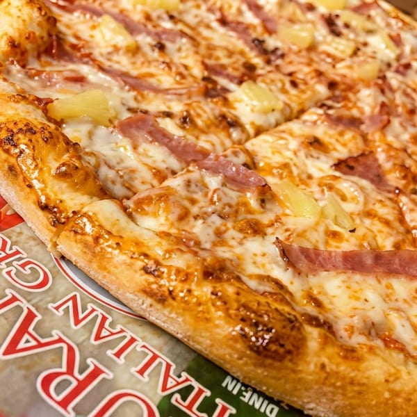 Hawaiian pizza with ham and pineapple slices on a delivery box, close-up.