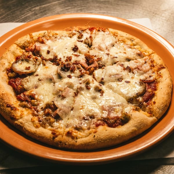 A freshly baked, sliced pizza with melted cheese, mushrooms, and bacon on an orange plate.