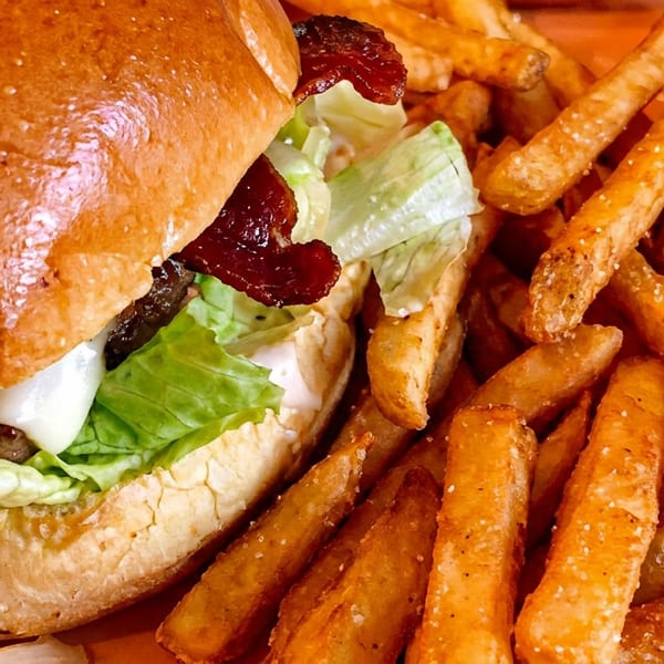 A close-up of a juicy bacon cheeseburger with lettuce and a side of golden, salted french fries.