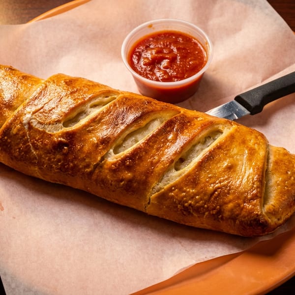 Golden-brown calzone with sauce and a knife on parchment paper, on an orange plate.